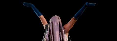 oachim Maudet sur scène, de dos, dansant en slip et portant un vêtement sur sa tête et des chausettes bleu foncées sur ses deux avant-bras