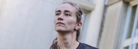 Portrait de la danseuse Annaelle Toussaere, les cheveux blond cendrés, attachées, portant un t shirt noir et un jeans de couleur brute les bras tombant