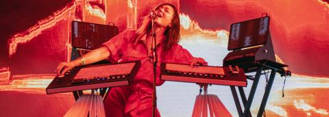 Photo de DeLaurentis sur scène, on la voit habillée d'une combinaison rouge en train de chanter et de jouer