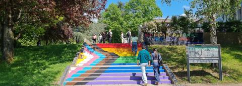 Des personnes montent les escaliers peint au couleurs du drapeau LGBTQIA+ de l'Université Rennes 2, sur le mûr en haut des marches on lit le message tagué "Nos fiertés plus fortes que leur haine".