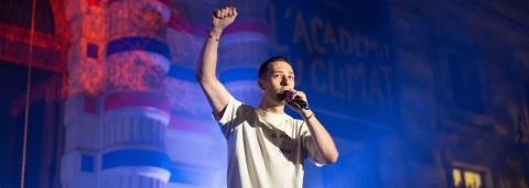 On y voit un homme tenant un micro de la main gauche et levant le bras gauche