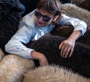 Visuel faire troupeau, photo de Marion Thomas, (au centre) portant des lunettes noires de soleil, entourée de d'un troupeau de moutons