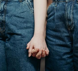 Photo en plan rapproché où on y voit deux femmes en jeans se tenir la main 