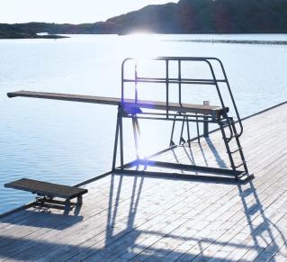 Photographie d'un plongeoire au bord d'une piscine avec en fond un ciel bleu et le reflet du soleil sur l'eau