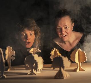Deux femmes regardent des figurines en carton placés devant elles.
