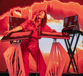 Photo de DeLaurentis sur scène, on la voit habillée d'une combinaison rouge en train de chanter et de jouer