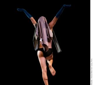 Joachim Maudet sur scène, de dos, dansant en slip et portant un vêtement sur sa tête et des chausettes bleu foncées sur ses deux avant-bras