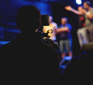 Une personne se trouve derrière une caméra et film des personnes sur scène