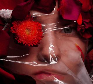 photo d'une femme dont on voit le visga derrière un plastique transparent, avec des fleurs et des pétales devant. La photo illustre la claustrophobie, qui est le nom de la photo