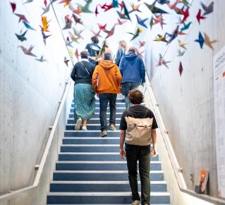 Photo prise dans la salle l'Antipode, on y voit des oiseaux faits en orgigami accroché en hauteur, des personnes montent des escaliers lors d'une visite du lieu