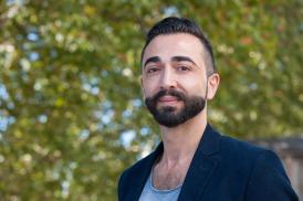Portrait de Reza Zia-Ebrahimi, portrant un costard bleu, regardant l'objectif avec derrière lui des arbres en fond