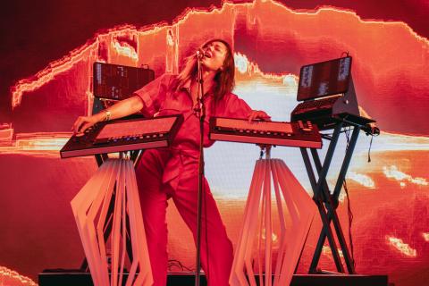 Photo de DeLaurentis sur scène, on la voit habillée d'une combinaison rouge en train de chanter et de jouer