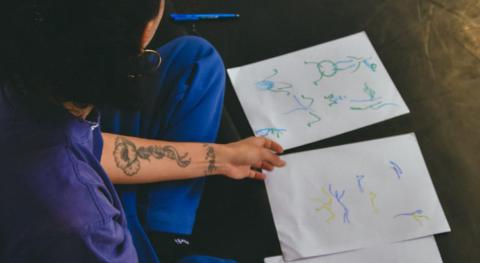 Une personne avec un crayon dans la main avec des feuilles devant elle dessine des mouvements de danse