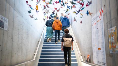 Photo prise dans la salle l'Antipode, on y voit des oiseaux faits en orgigami accroché en hauteur, des personnes montent des escaliers lors d'une visite du lieu