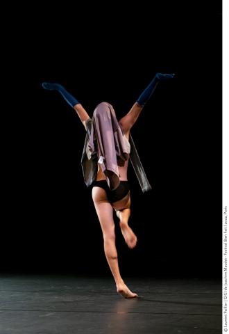 Joachim Maudet sur scène, de dos, dansant en slip et portant un vêtement sur sa tête et des chausettes bleu foncées sur ses deux avant-bras