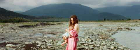 photo de Noé représentant une femme en robe rose donnant le sein à un enfant avec les montagnes en arrières-plan 