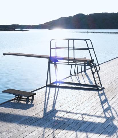 Photographie d'un plongeoire au bord d'une piscine avec en fond un ciel bleu et le reflet du soleil sur l'eau