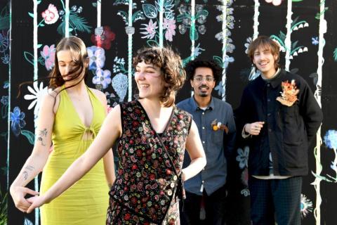 A Toda Hostia, groupe de quatre jeunes adultes, deux femmes à gauche de la photo, deux hommes à droite de la photo, souriantes et souriants devant un mur à fond noir avec des motifs floraux colorés.