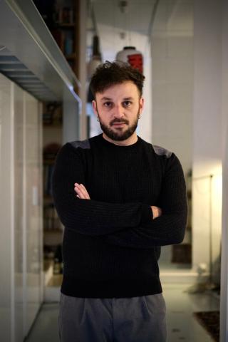 Photo de l'ariste Romuald Jandolo coirsant ses bras et fiaxant droit devant lui, il est habillé tout en noir et porte des créoles à chacune de ses oreilles.