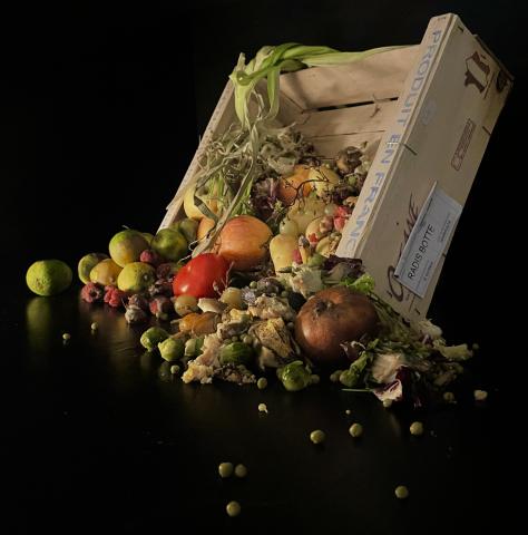 Photographie de fruits et légumes tombant d'une cagette en bois sur fond noir